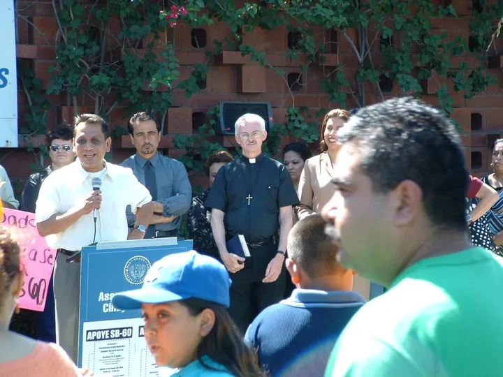 Speakers and community members at a rally with a priest and families